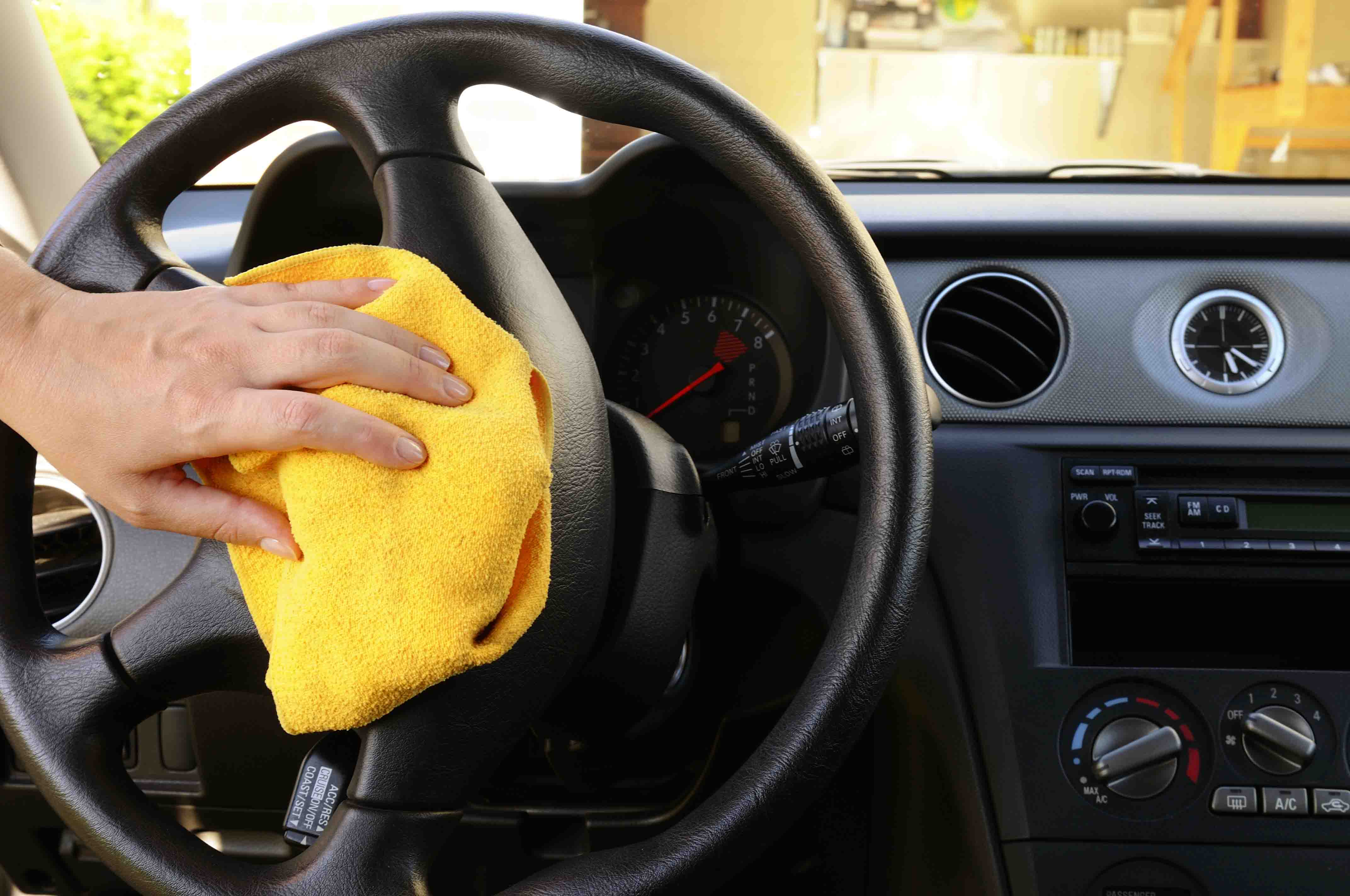 Woman's nand with microfiber cloth polishing steering wheel of an SUV car